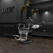 DIR Vanquish Professional Barbershop Chair Black Variant Front Angled View With Mirror A Brand Name And A Deer Head Sculpture In The Background