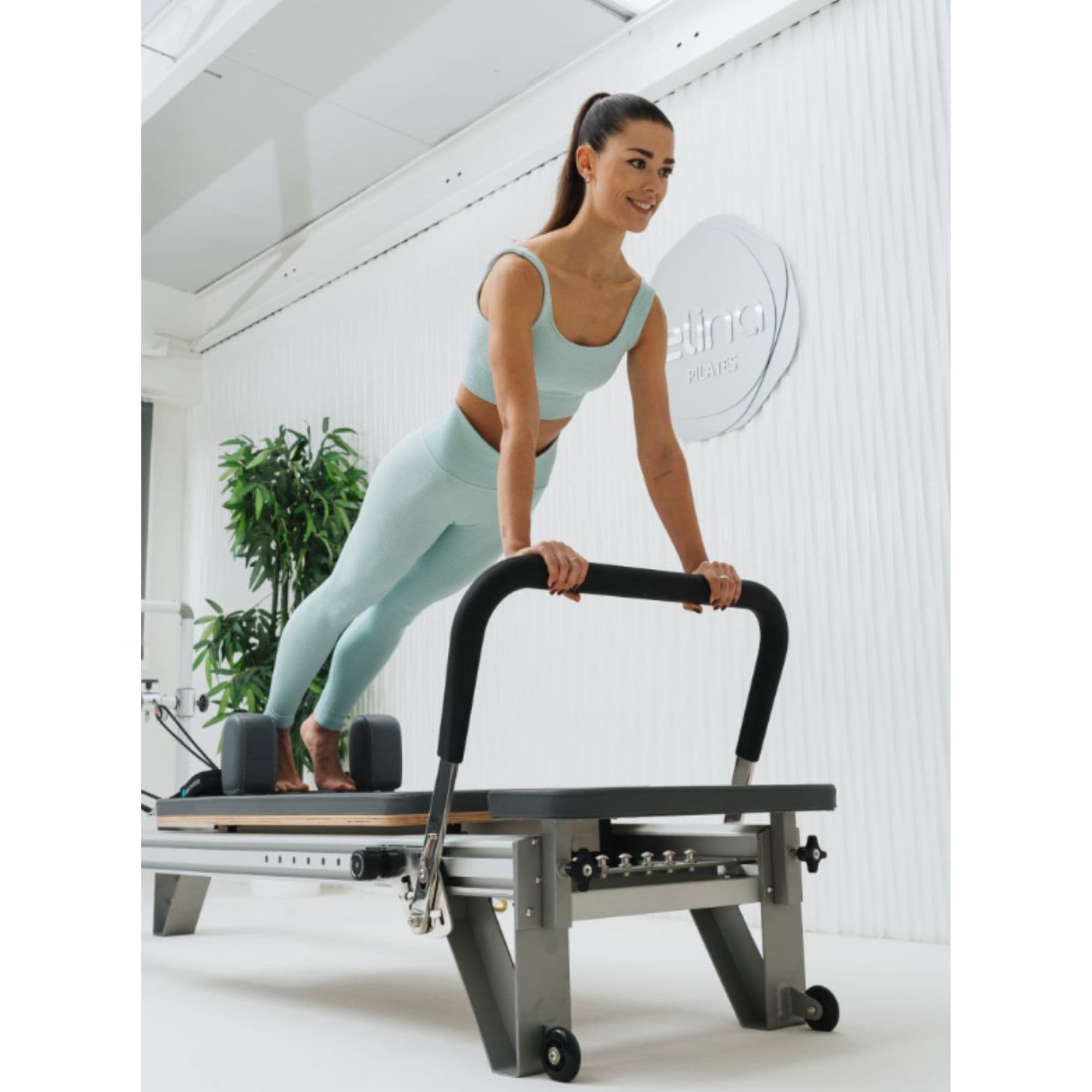Elina Aluminium Reformer Mentor With A Woman Performing A Push-up Exercise And Potted Green Plants In The Background