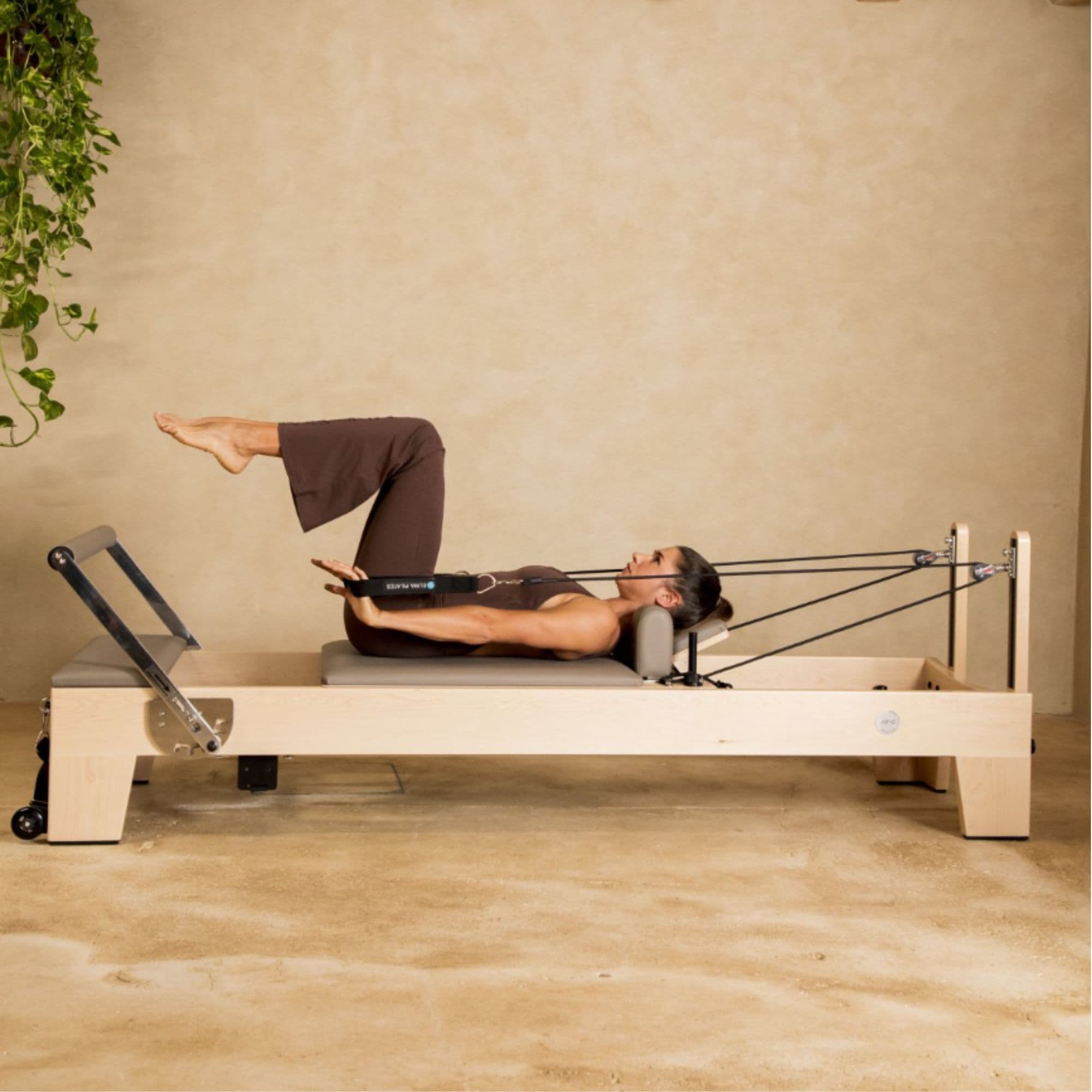 Elina Elite Wood Reformer Gray Variant With Woman Demonstrating Pilates While Pulling The Rope Pulley