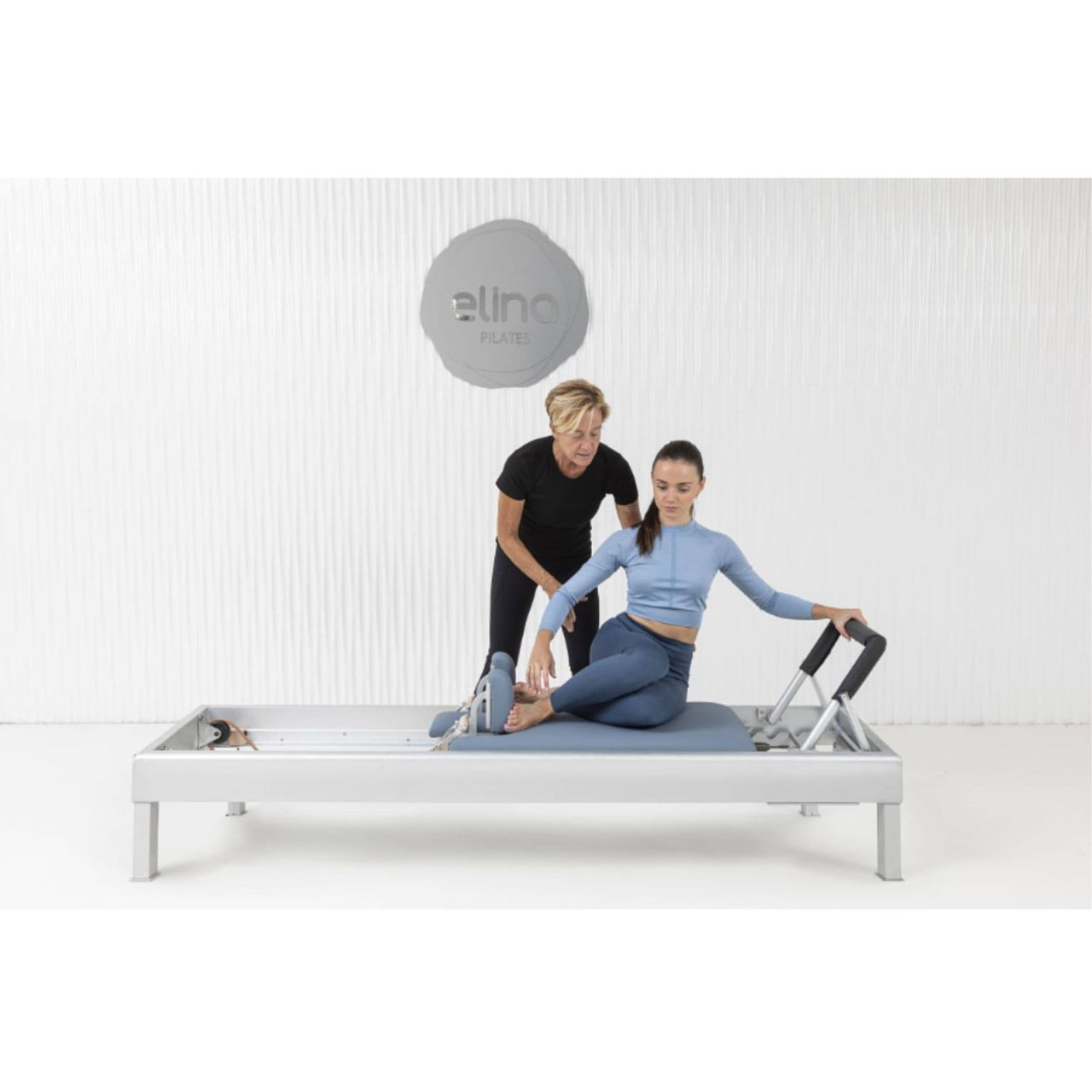 Elina Pilates Classic Aluminium Reformer 86 Inches With One Older Woman Assisting The Young Girl While Performing The Exercise