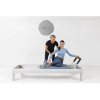 Thumbnail for Elina Pilates Classic Aluminium Reformer 86 Inches With One Older Woman Assisting The Young Girl While Performing The Exercise