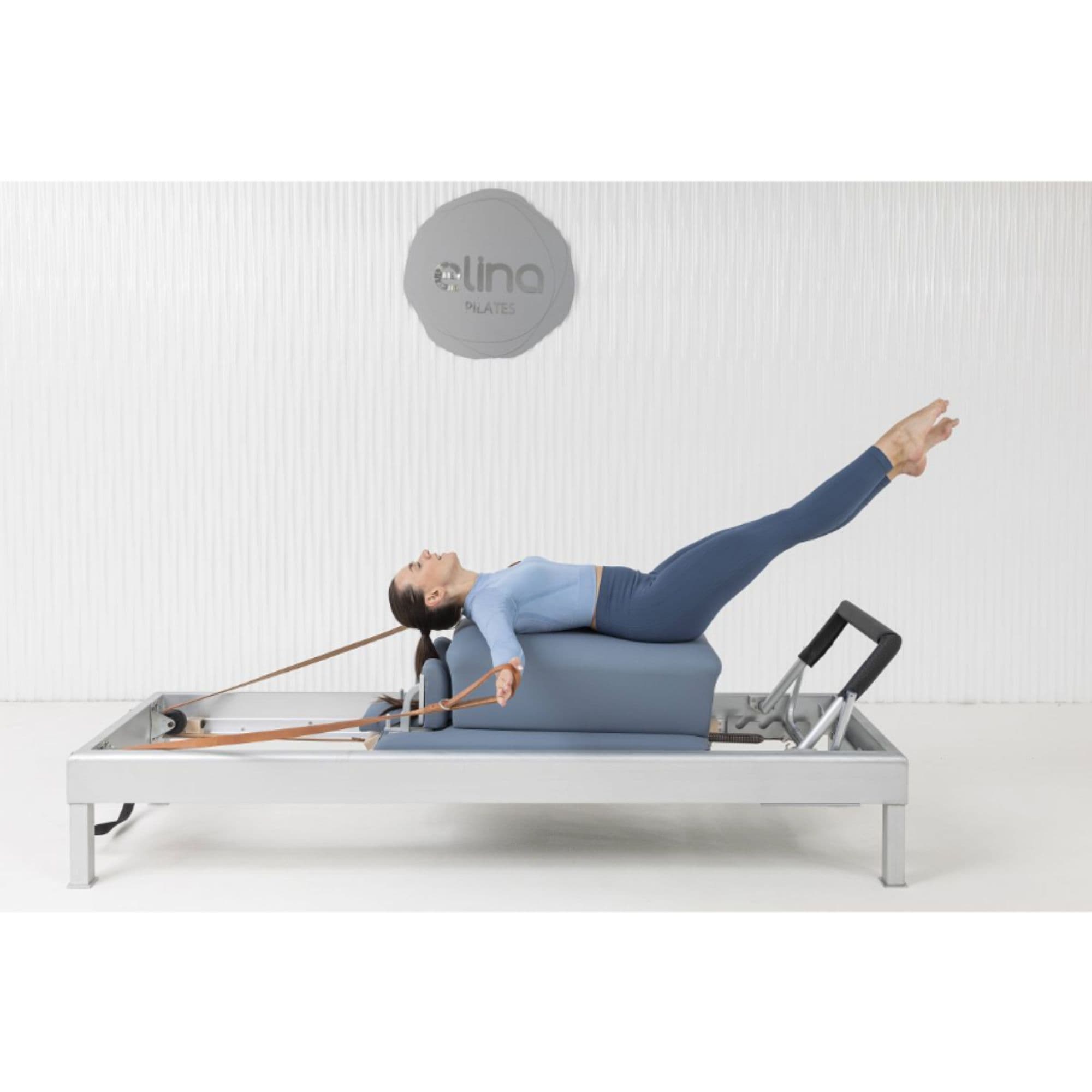 Elina Pilates Classic Aluminium Reformer With A Woman Performing Exercise While Raising Her Both Legs While Using A Leather Straps