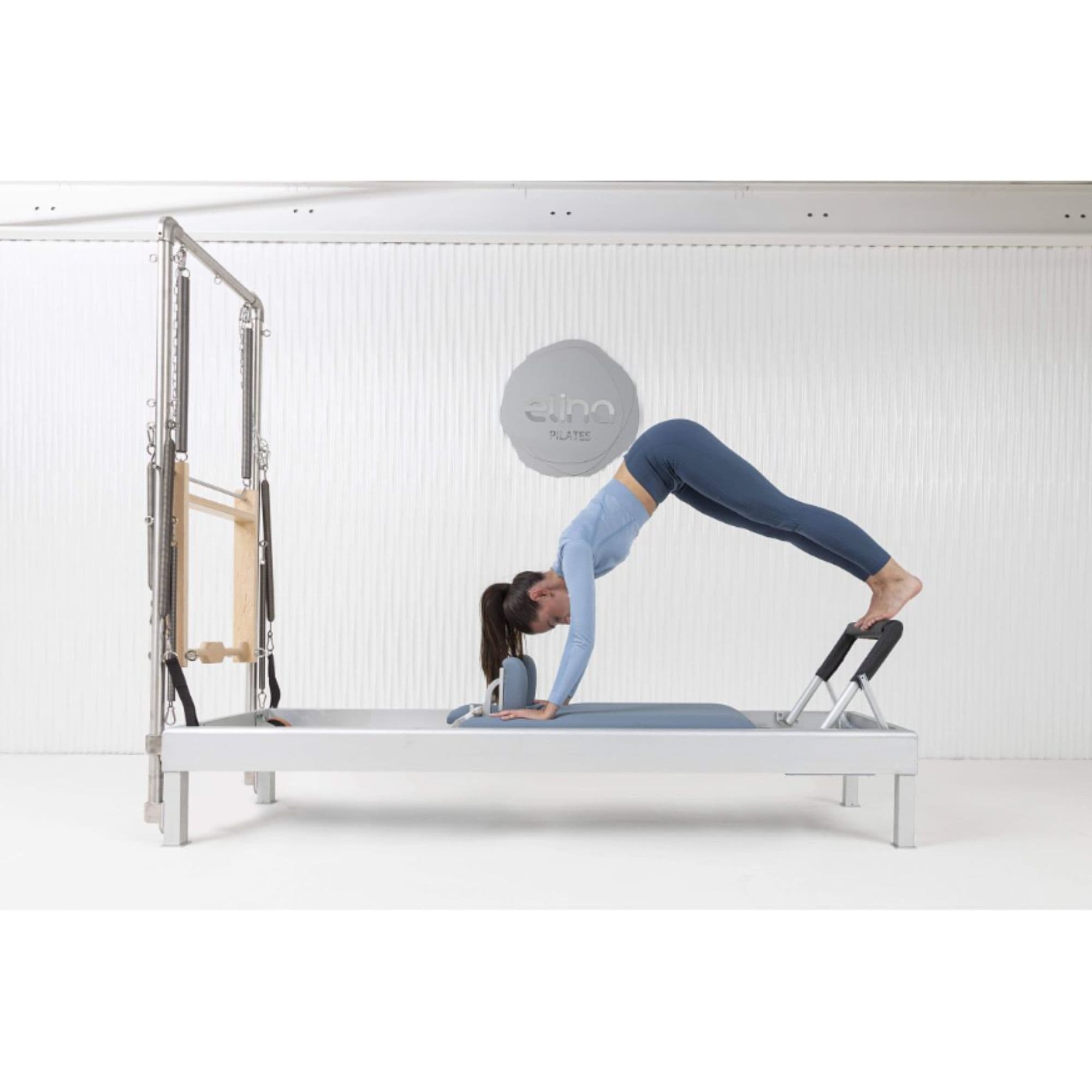 Elina Pilates Classic Aluminum Reformer & Tower Inches With A Woman Performing Exercise Using The Footbar