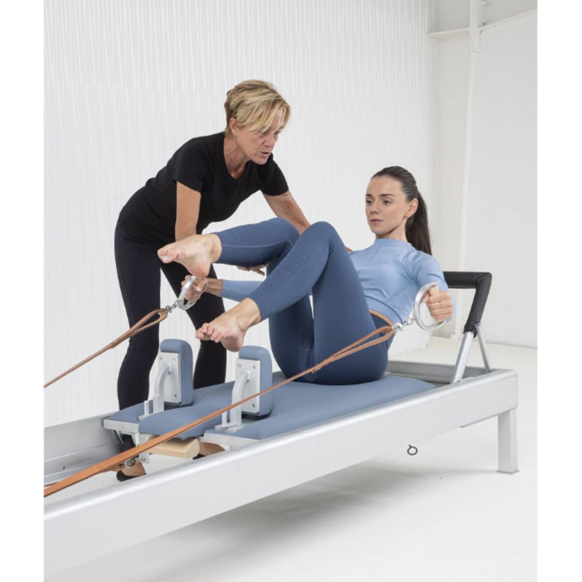 Elina Pilates Classic Reforming 86 Inches With An Older Woman Assisting The Young Girl While Performing The Exercise Using The Leather Straps