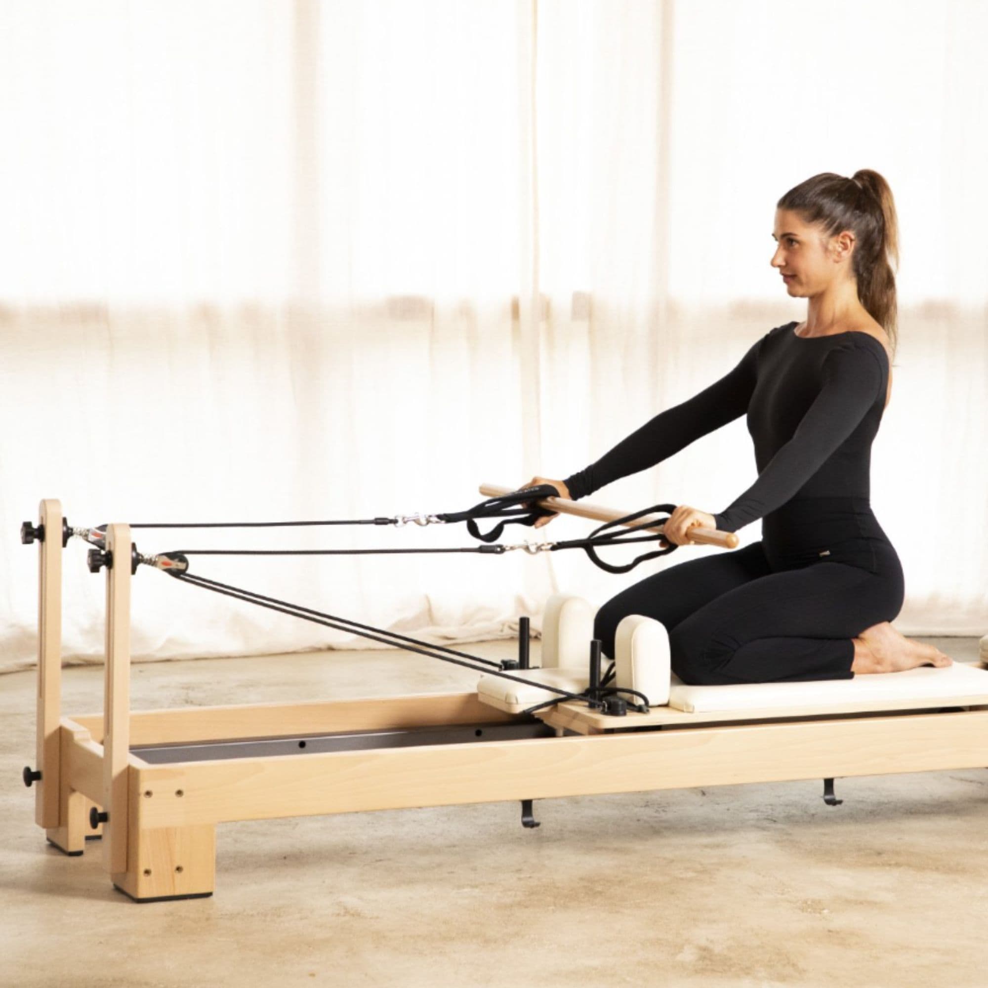 Elina Pilates Lignum Wood Reformer With A Woman Demonstrating An Exercise Using A Resistance Strap