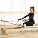 Elina Pilates Lignum Wood Reformer With A Woman Demonstrating An Exercise Using A Resistance Strap