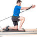Elina Pilates Physio Reformer Master Instructor With A Man Performing A Half-Kneeling Pilates Resistance Exercise Using An Arm Strap