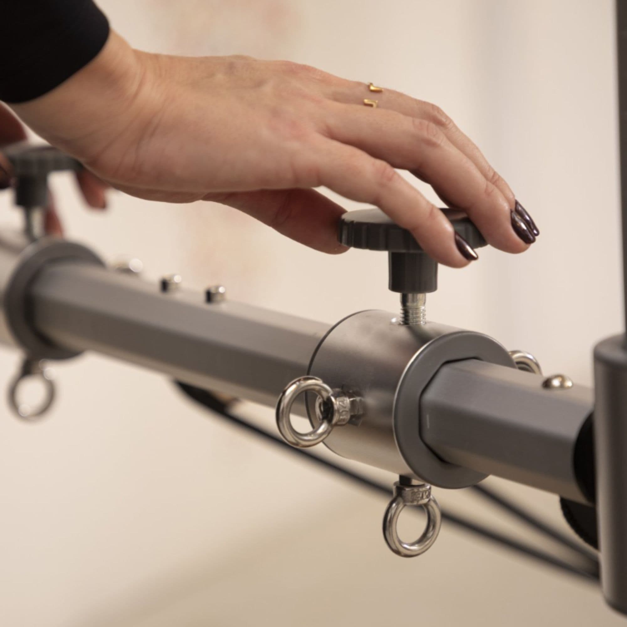 Elina Pilates Reformer Master Instructor With A Hand Adjusting Tower Crossbar Locking Knob On White Background