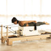 Elina Pilates Wooden Reformer Ligno Side View Of A Woman Demonstrating A Long Box Exercise And A Resistance Strap