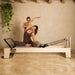 Elite Wood Reformer Gray Variant With Woman Demonstrating Pilates And With Instructor