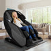 Infinity Imperial Massage Chair Certified Pre-Owned Dark Front Angled View With A Woman Relaxing In A Modern Living Room Setting