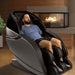 Kansha M878 Massage Chair Front Angled View If A Man Relaxing In A Modern Home Setting With Fireplace And Potted Plant Background