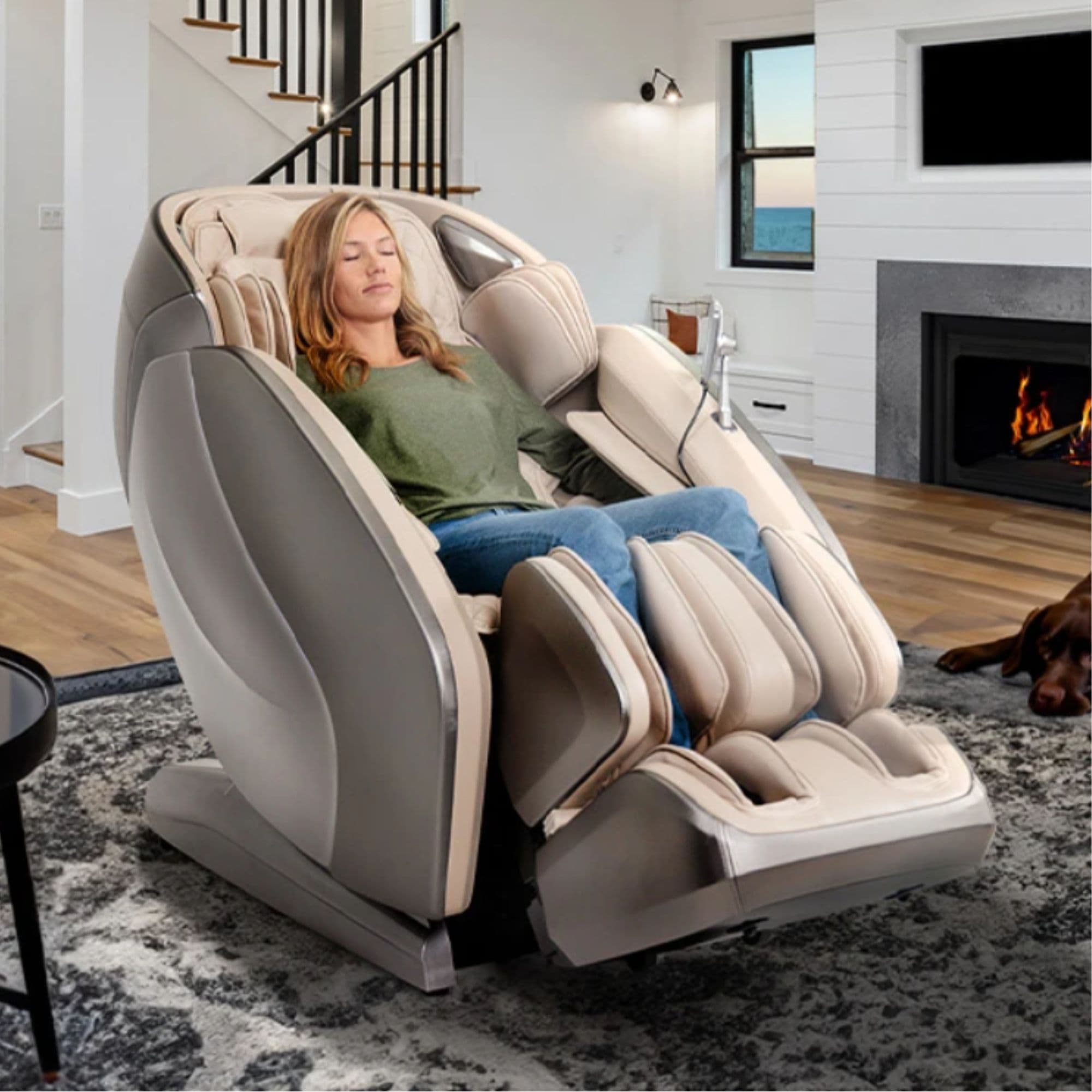 Kyota Hatsumei M900 4D AI Massage Chair Gray Tan Variant Front Angled Lifestyle View Of A Woman Relaxing In A Pet-Friendly Living Room With A Fireplace