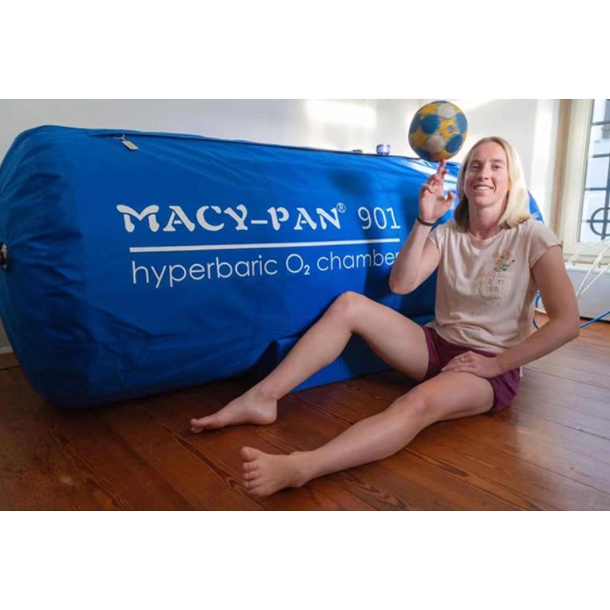 Macy-Pan ST901 1.3 to 1.4 ATA Soft Lying Hyperbaric Chamber Front Angle View With A Man Sitting On The Wooden Floor While Holding A Ball