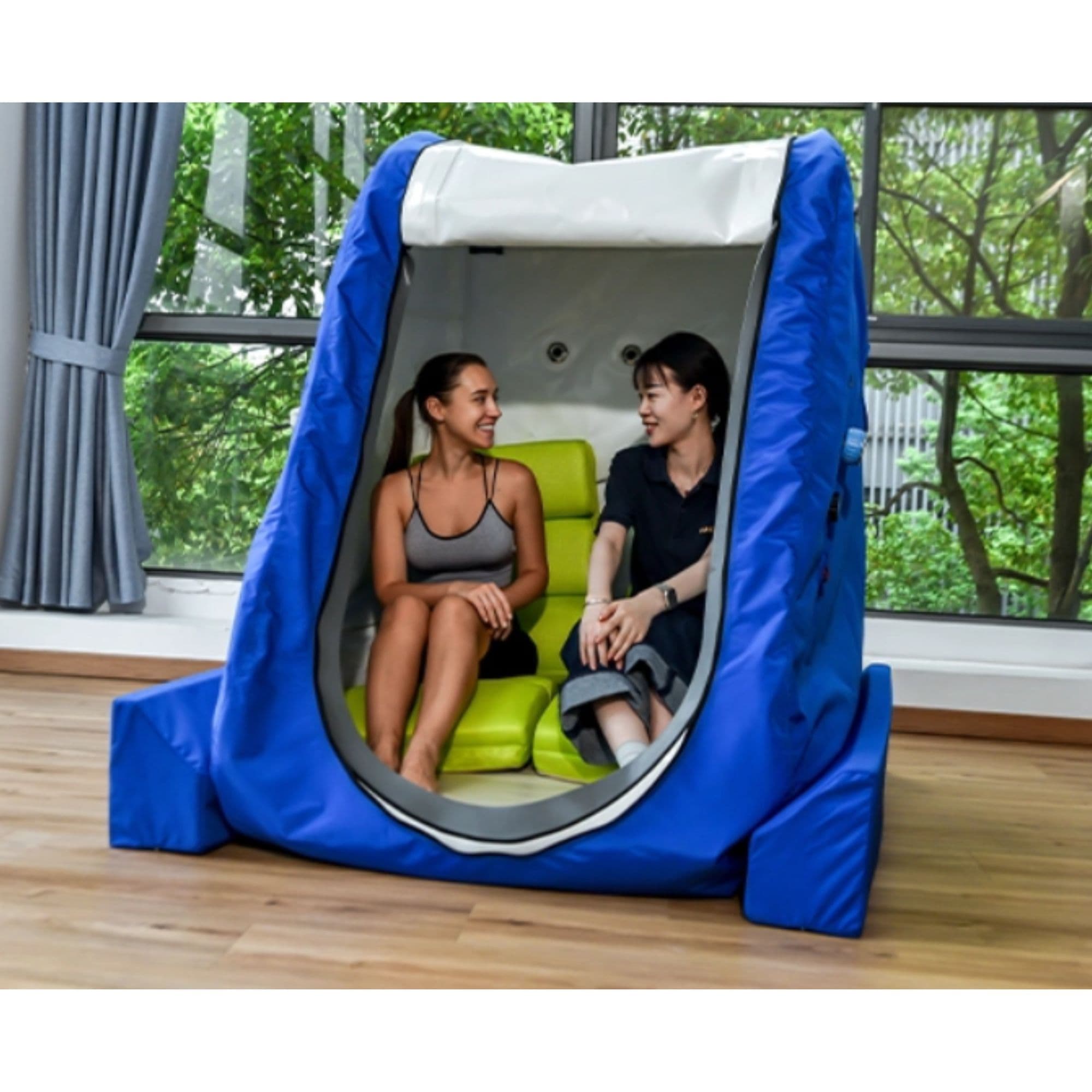 Macy Pan MC4000 Double-Sitting Hyperbaric Chamber Open Door Angle View Of Blue Color With Two Ladies Inside In Large Windows And Greenery View