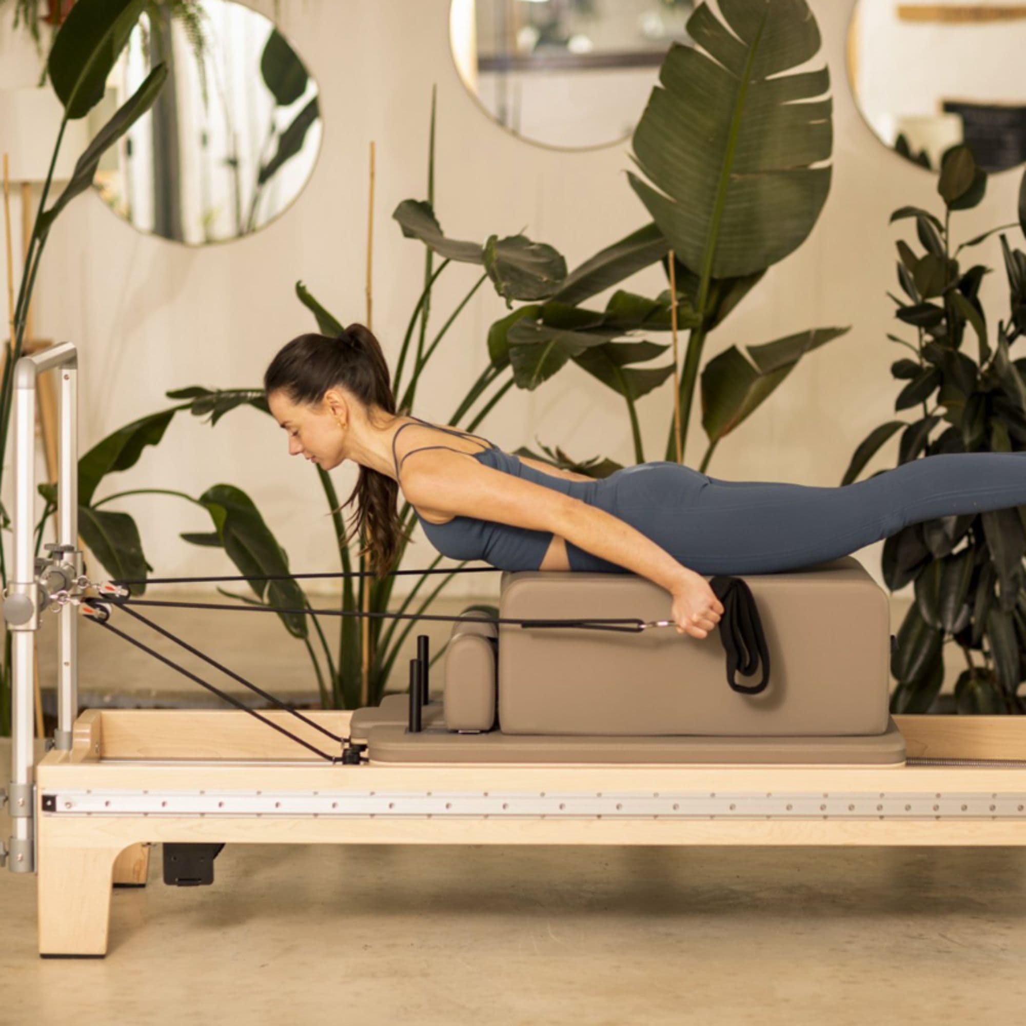 Reformer Master Instructor Side View Of A Woman Performing A Pilates Exercise On A Reformer With Tropical Green Plants In The Background