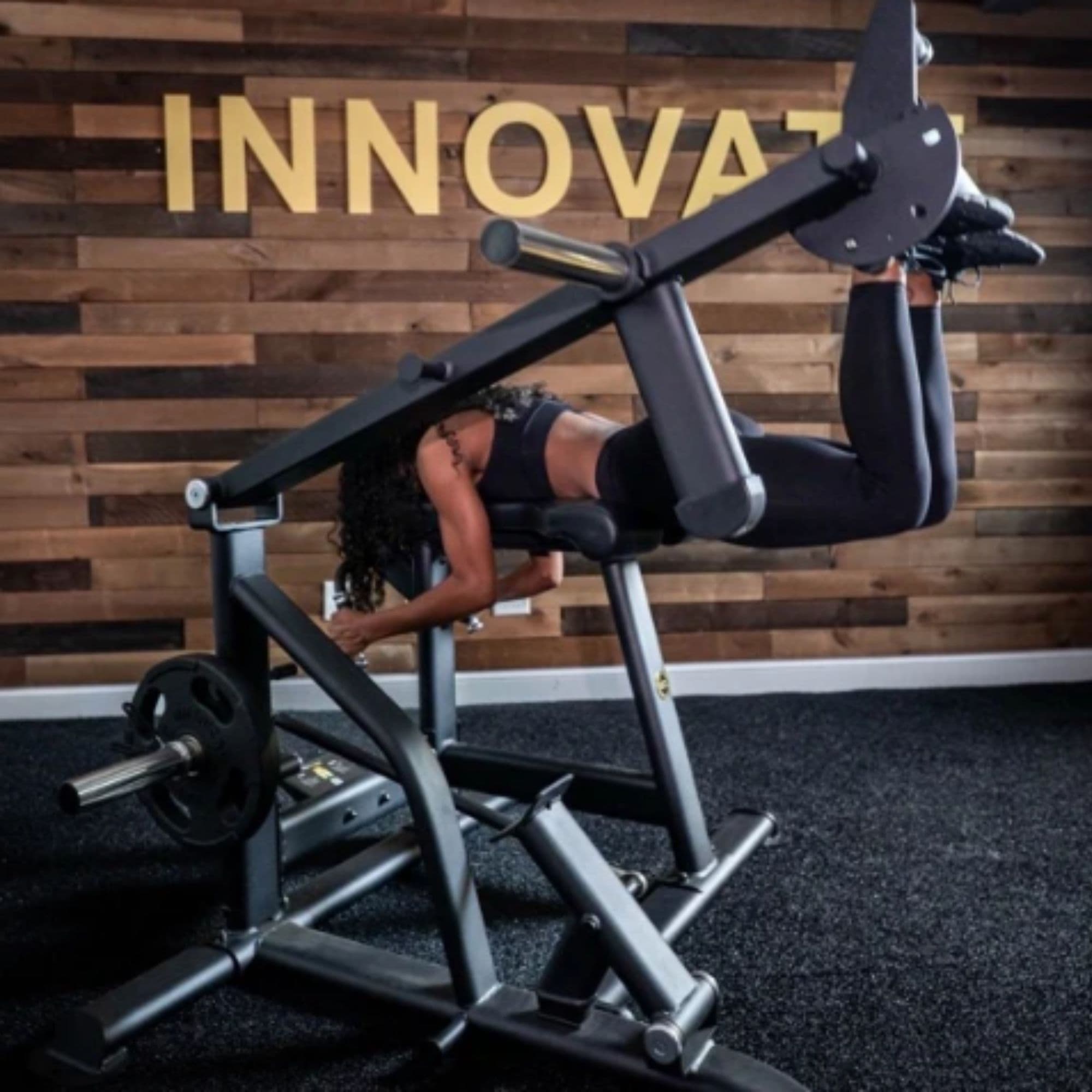 The Abs Company Froggy Hip Thrust Bench Side View Of A Woman Performing A Prone Leg Curl With Wooden Wall Background