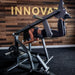 The Abs Company Froggy Hip Thrust Bench Side View Of A Woman Performing A Prone Leg Curl With Wooden Wall Background