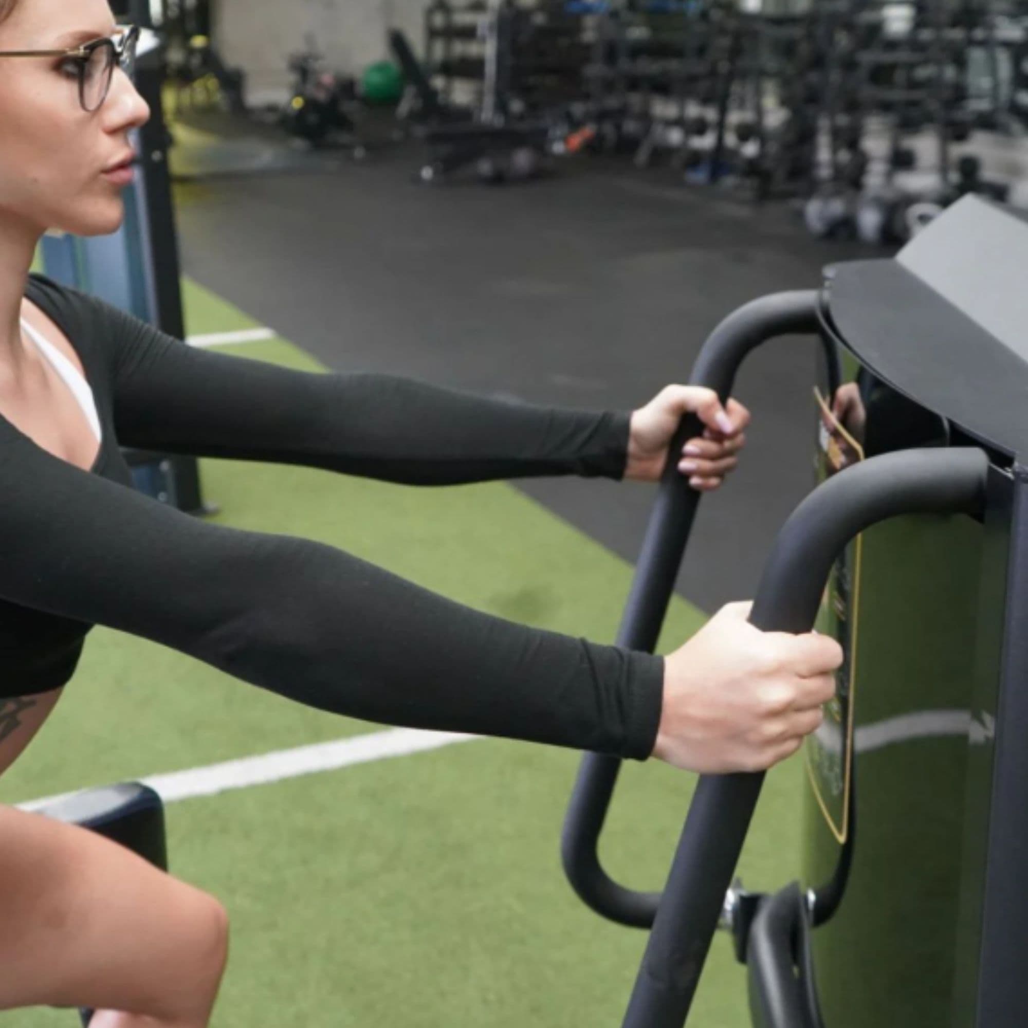 The Abs Company Total Glute With A Woman Holding The Handles On A Gym Setting