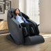Yugana M780 Massage Chair Black Variant Front Angled View Of A Woman Relaxing Near Large Windows With White Curtains